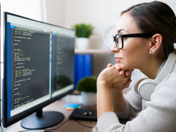 Woman focused on coding at her computer with headphones around her neck.