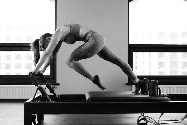Woman performing Pilates on a reformer machine in workout attire.