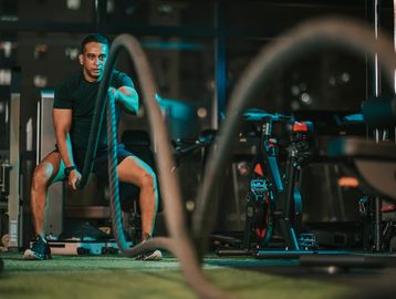 Man intensely working out with battle ropes in a gym at night.