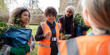 Group of women in safety vests holding plants outdoors.