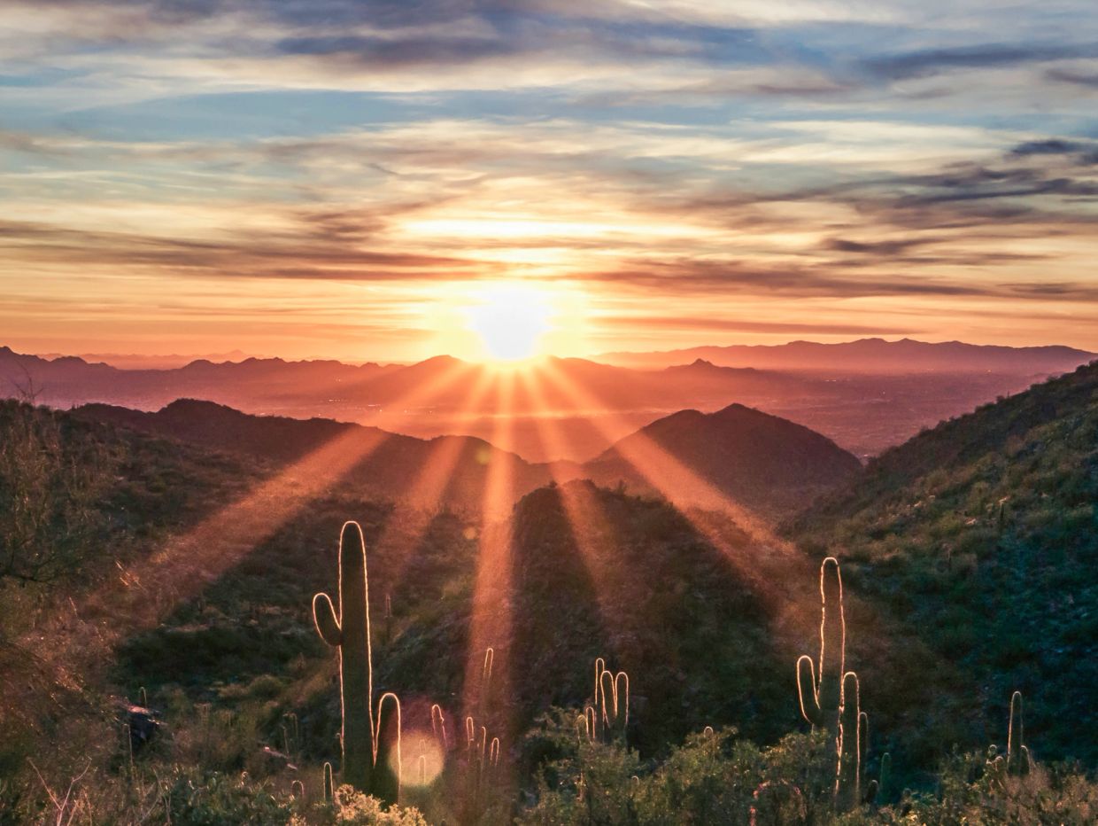 Sunset casting golden rays over desert mountains and cacti.