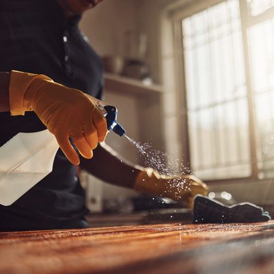 Person cleaning wooden surface with spray bottle.