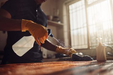 Person wearing gloves cleaning a surface with a spray bottle.