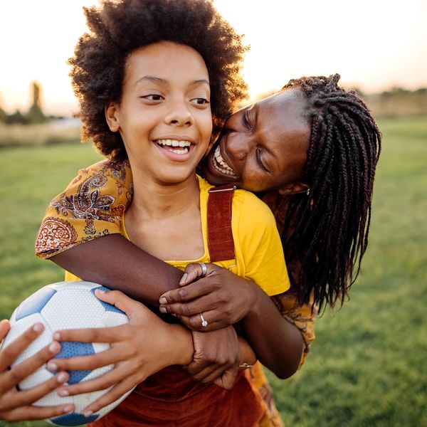 A joyful moment between a woman and child holding a soccer ball outdoors.