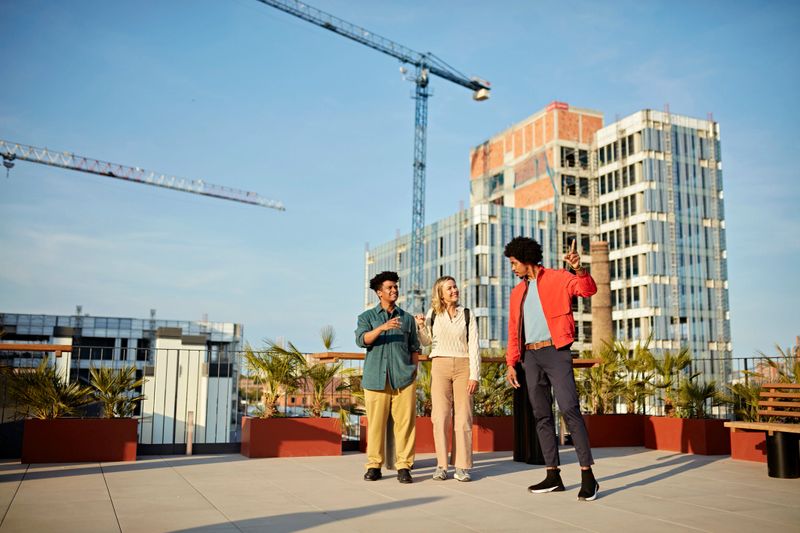 Full length front view of clients and broker enjoying view from deck atop office building with construction cranes and development in background.