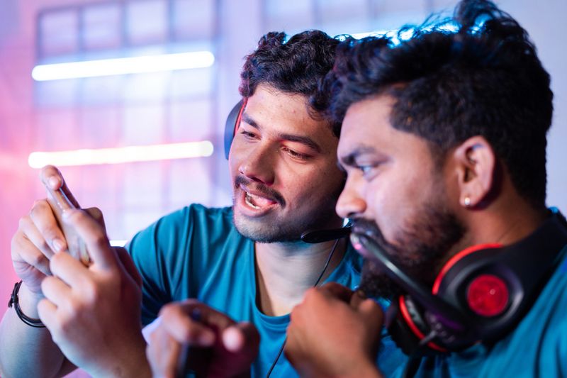 Two gamers discussing about game play by looking into mobile phone at esports championship league - concept of teamwork, strategy, togetherness and in multi-player tournament