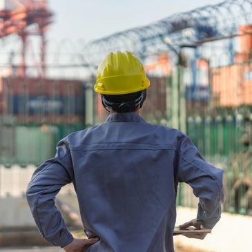 Construction worker in a yellow helmet inspecting an industrial site importing goods at harbour