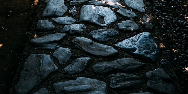 A stone pathway with irregularly shaped dark stones under dappled light.