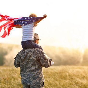 Soldier carrying child with American flag on shoulders.