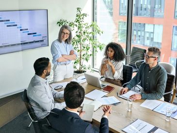 A group of professionals engaged in a business meeting with a project timeline on a screen.