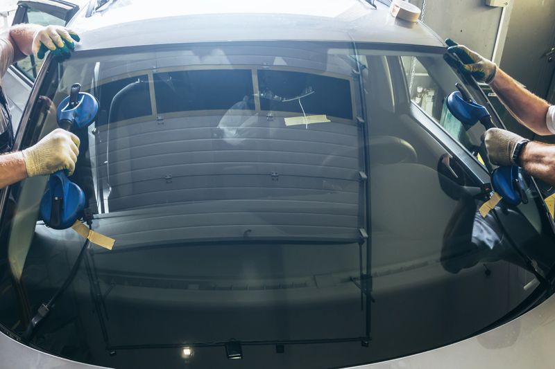Mechanic workers hands changes broken windscreen on new windshield on car in service station close up.
