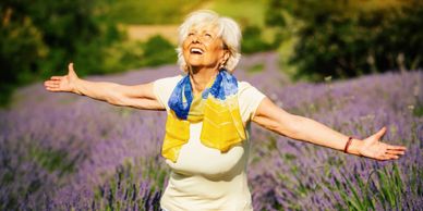 Joyful elderly woman enjoying a sunny day in a lavender field.