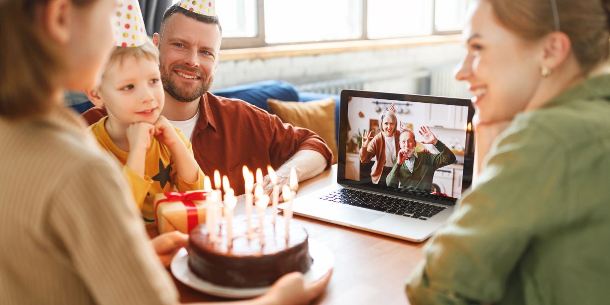 Family celebrating a birthday via video call with a cake and gifts.