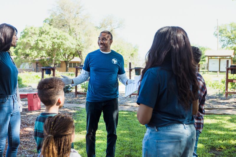 The mature adult male director welcomes a multi-ethnic group of volunteers to the community gardens.