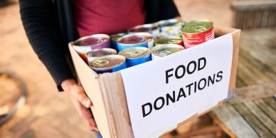 Person holding a box labeled 'Food Donations' with canned goods.