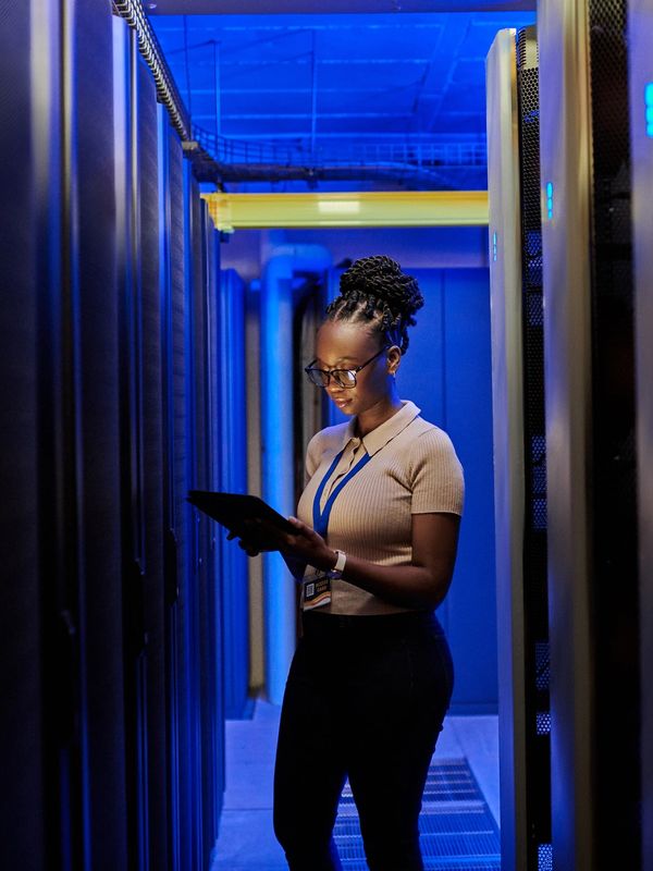 Woman working on a tablet in a blue-lit server room.