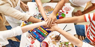 Group of people putting their hands together over art supplies.