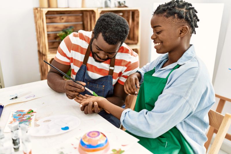African american painter couple smiling happy painting hands sitting on the table at art studio.
