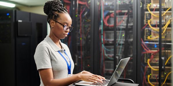 Woman working on a laptop in a server room.