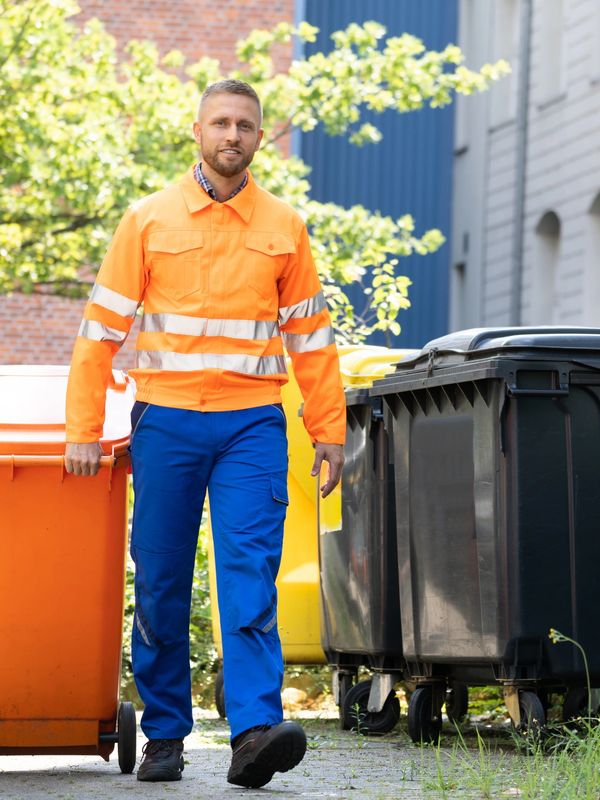 A valet trash worker is pulling a trash can for valet trash collection.