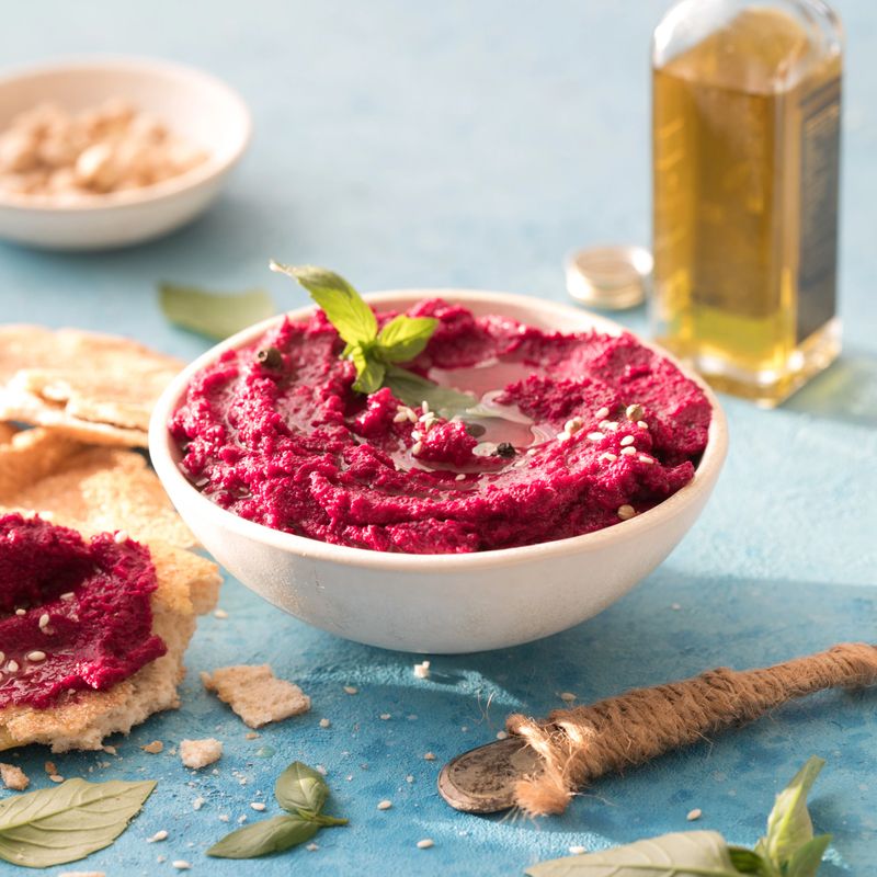 red beetroot hummus on blue background, lemon, sesame, olive oil, pita. Middle eastern, jewish, arabic cuisine.
