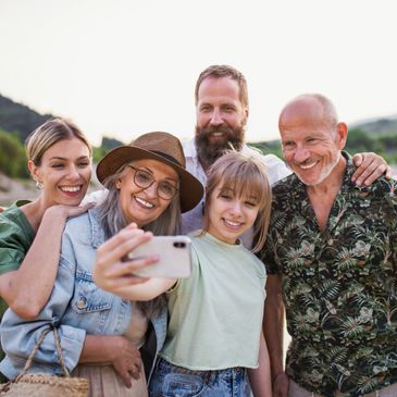 A joyful multi-generation family takes a selfie outdoors by the water.