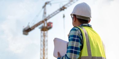 Construction worker with hard hat and safety vest reviewing plans at site.