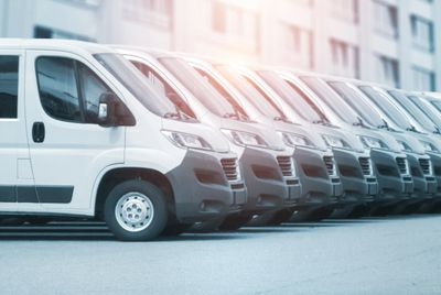 A row of white delivery vans parked in a line outside.