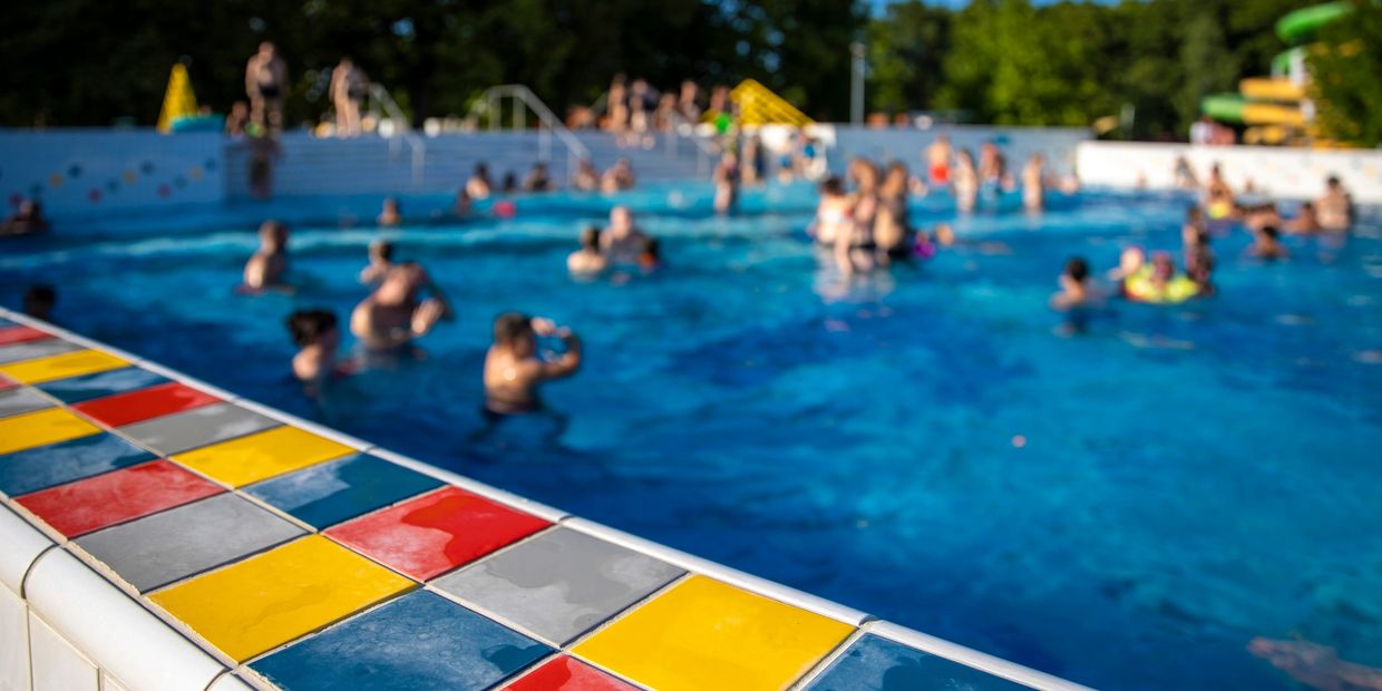 A large public swimming pool with swimmers and colorful tile edging on a sunny day