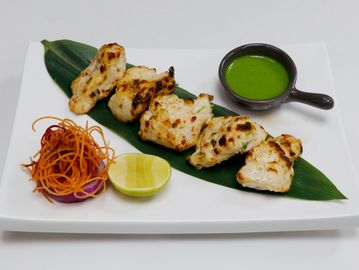 Grilled chicken pieces served on a leaf with green chutney, lemon, and shredded vegetables.