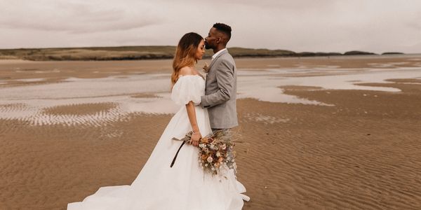 Bride and groom share a tender moment on a sandy beach.