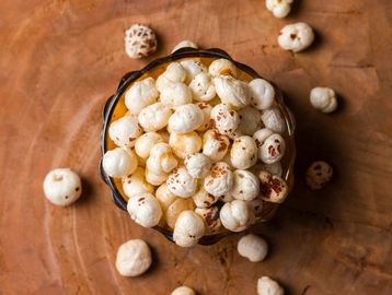 Bowl of popped fox nuts on wooden surface.