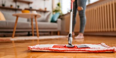 Person mopping a shiny wooden floor in a cozy living room.