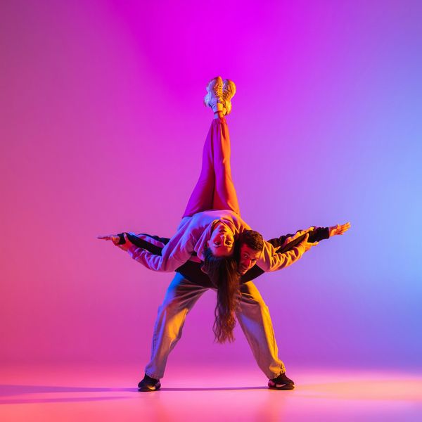 Two dancers performing an acrobatic pose with colorful lighting.