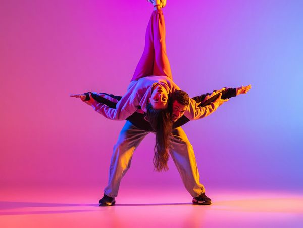 Two dancers performing an acrobatic pose with colorful lighting.