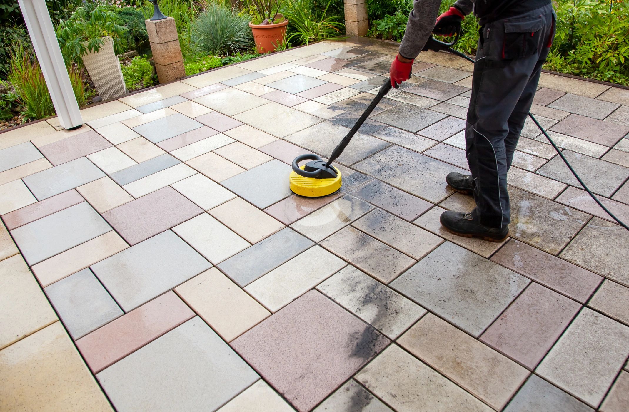 Person pressure washing a tiled patio to remove dirt and grime.