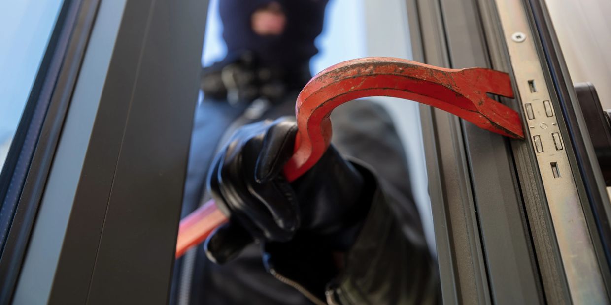 Masked intruder attempting to pry open a door with a crowbar.