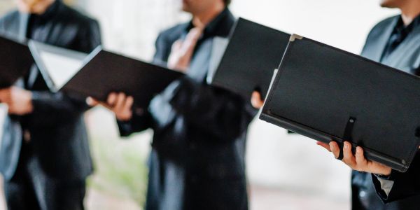 People in suits holding open folders, possibly singing or presenting.