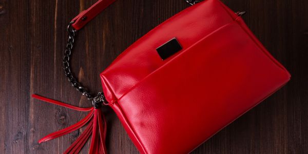 Sleek red leather handbag with tassel detail on wooden surface.