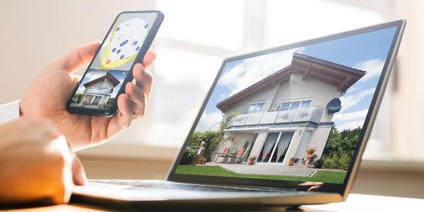 Person holding phone while browsing for real estate property on laptop