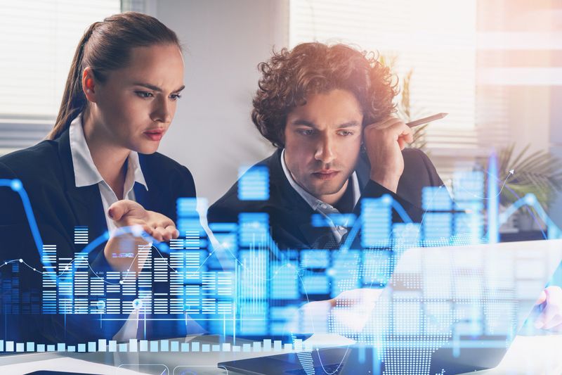 Business woman trader and businessman in formal suits is working together with financial report. Forex graph hologram foreground. Concept of trading and analytics.