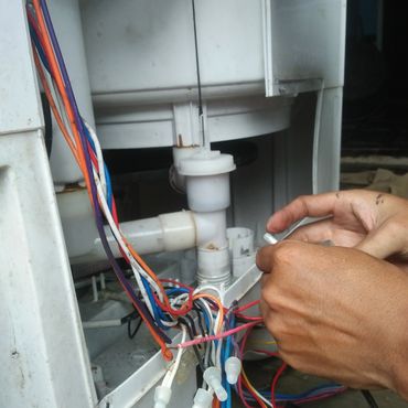 Hands working on colorful electrical wires inside a white appliance.