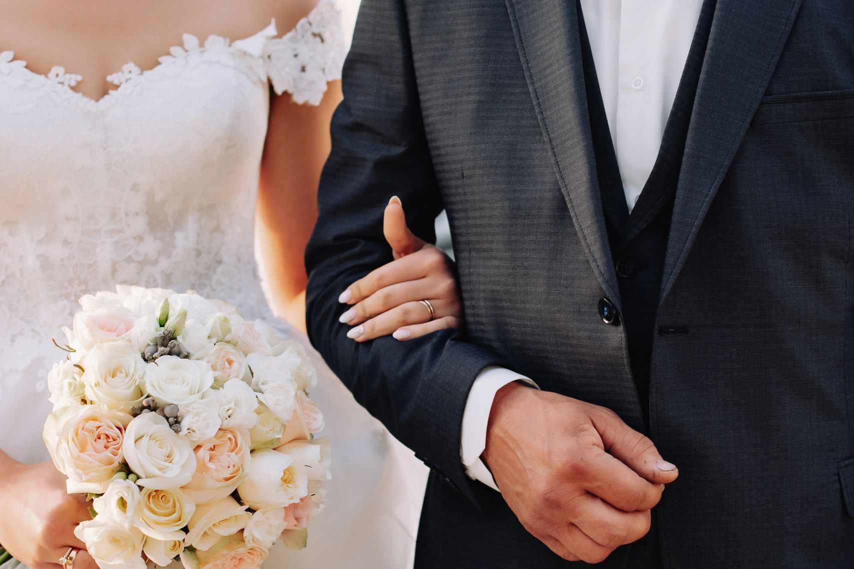 Bride in white gown holding bouquet, groom in dark suit linking arms.
