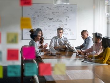 Diverse team collaborating around a table with colorful sticky notes and a business plan on the whiteboard.
