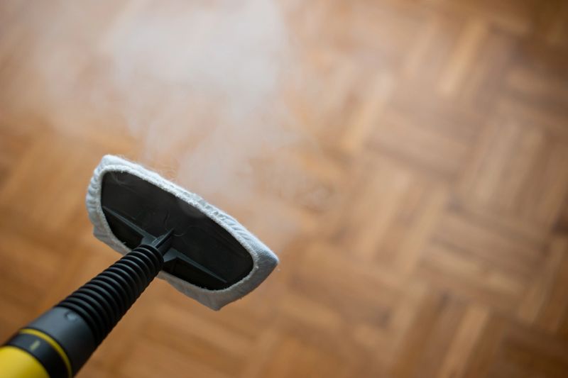 Steam pressure cleaner nozzle with cloth attachment. Cleaning and disinfecting against germs and viruses Close up studio shot, no people. Wooden tile floor, shallow depth of field.