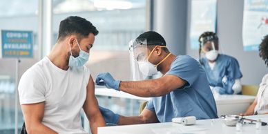 Healthcare worker administering a vaccine to a masked man in a clinic.