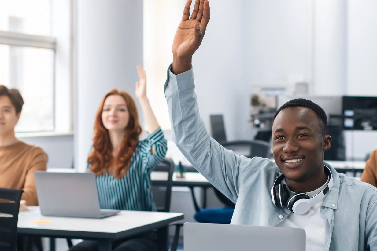 Students in a classroom happily raising their hands to participate.