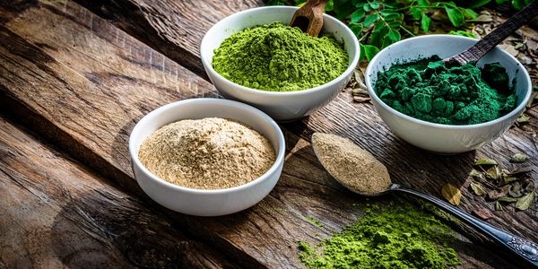 Three bowls with different colored herbal powders on a rustic wooden table.