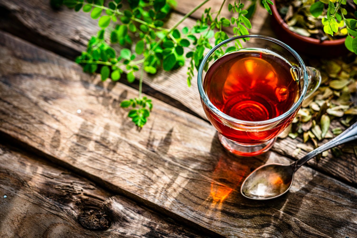 A cup of tea with leaves and a spoon on a rustic wooden table.