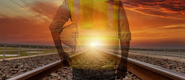 Construction worker superimposed on railway tracks at sunset.